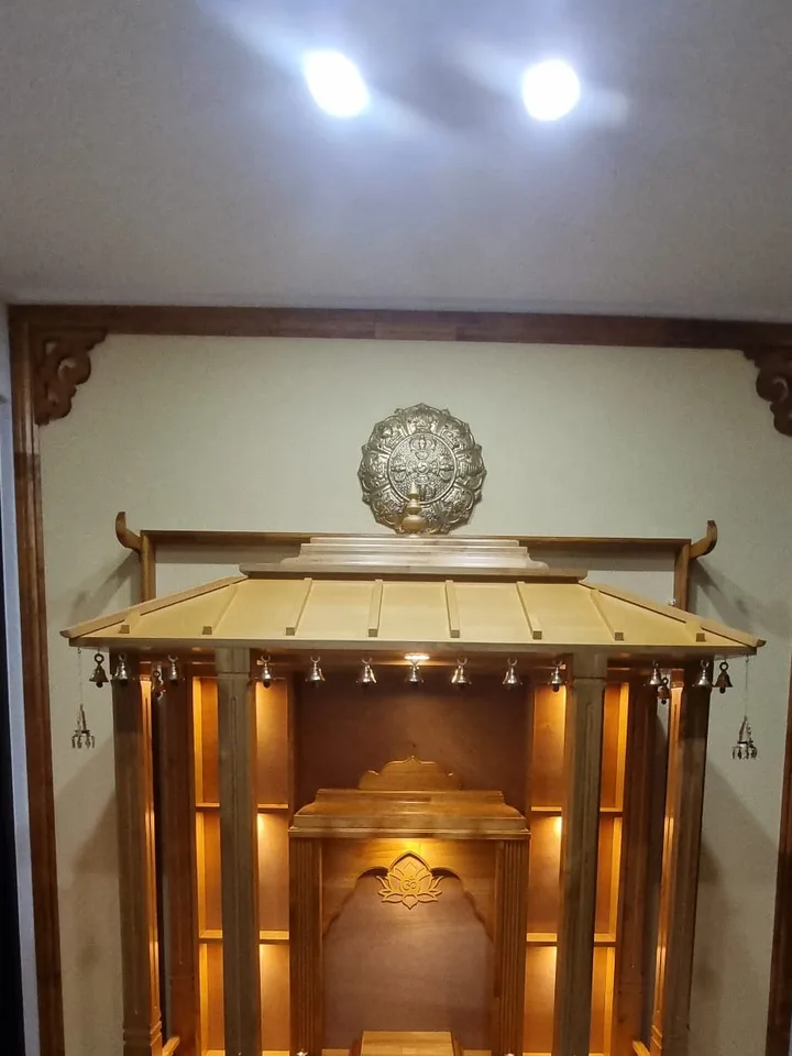 Large honey teak pagoda mandir with a wide gold roof and a row of brass bells along the eave