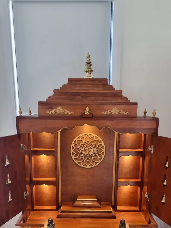 Brown Japan cabinet mandir with its bell-carved doors opened to reveal lit shelves