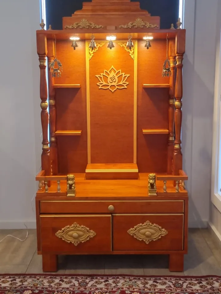 Honey teak mandir with a carved lotus om panel and gold-lined shelving