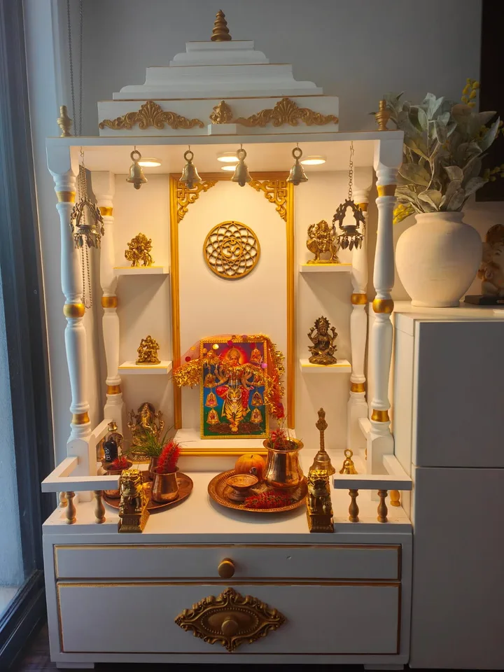 Ivory and gold mandir with fluted columns, brass bells and a full brass puja set on the platform