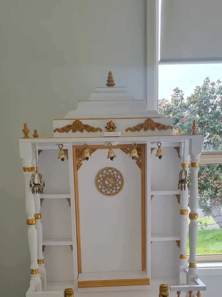 Ivory mandir with gold leaf detailing, hanging bells and paired guardian lions