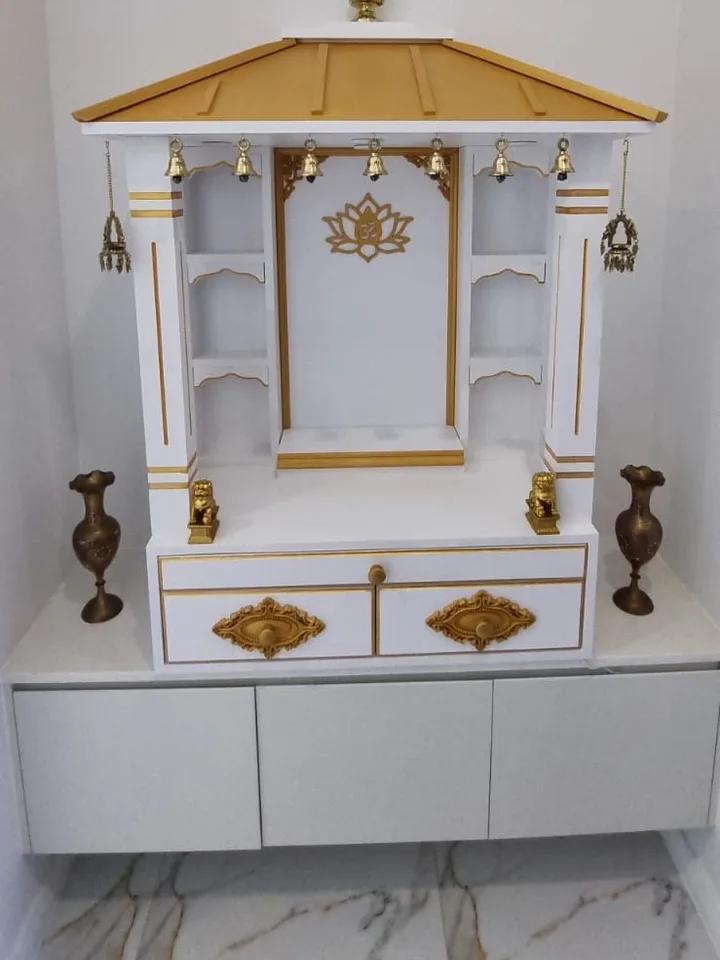 Ivory mandir with a gold pagoda roof set into a wall niche, flanked by brass vases